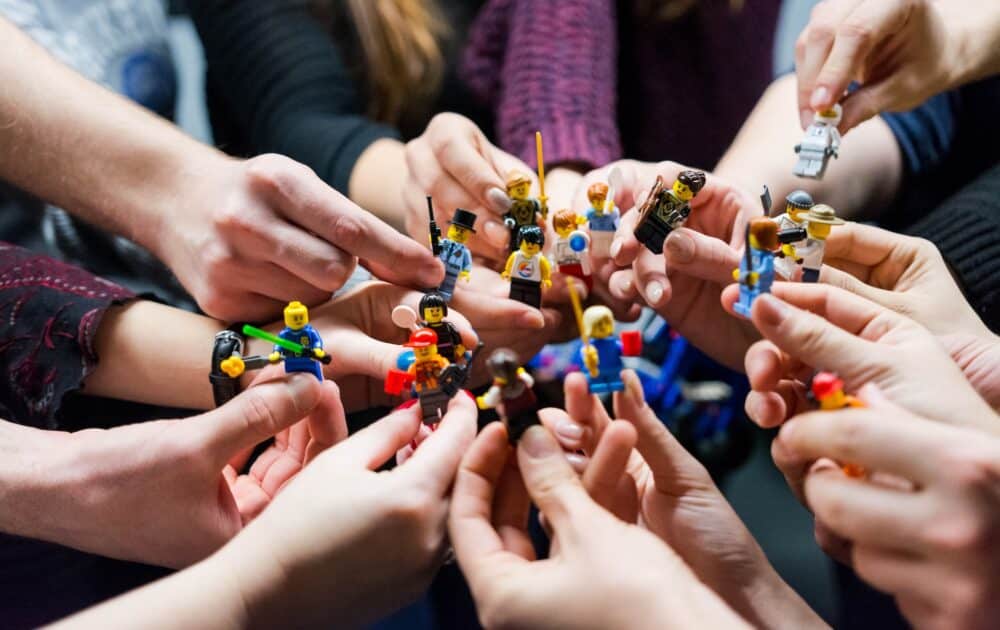 Haende halten diverse Legofiguren in die Mitte